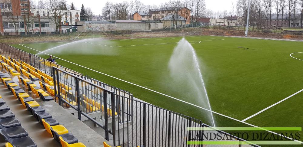 Automatiniai purkštuvai laisto futbolo aikštės veją šalia stadiono tribūnų