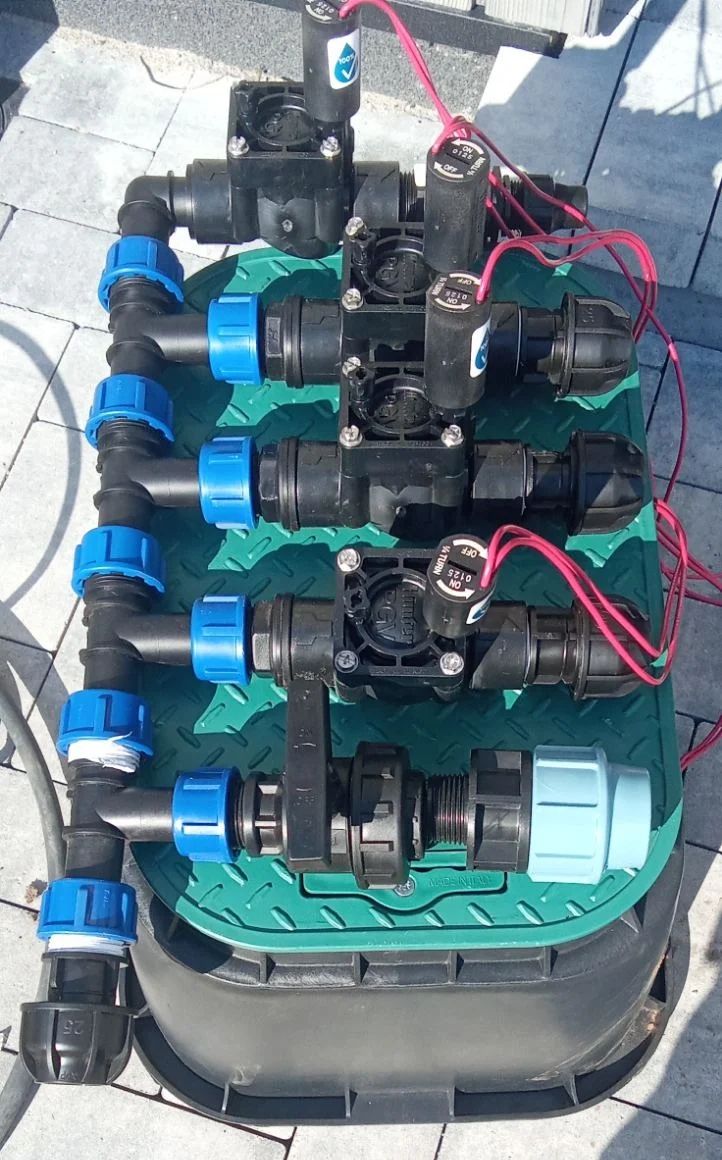 Elektromagnetinių laistymo vožtuvų mazgas su jungtimis ant žalio šulinėlio dangčio