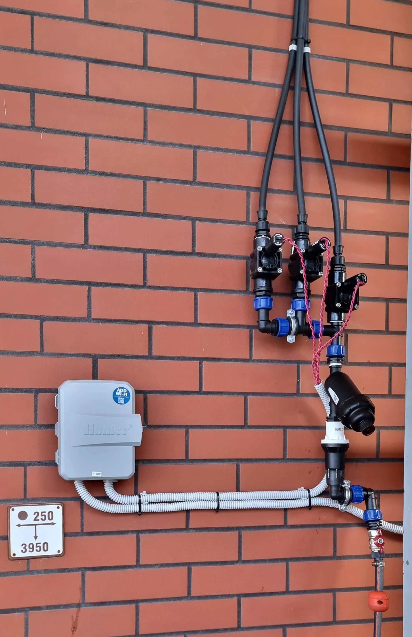 Hunter laistymo valdiklis ir elektromagnetiniai vožtuvai ant raudonų plytų sienos
