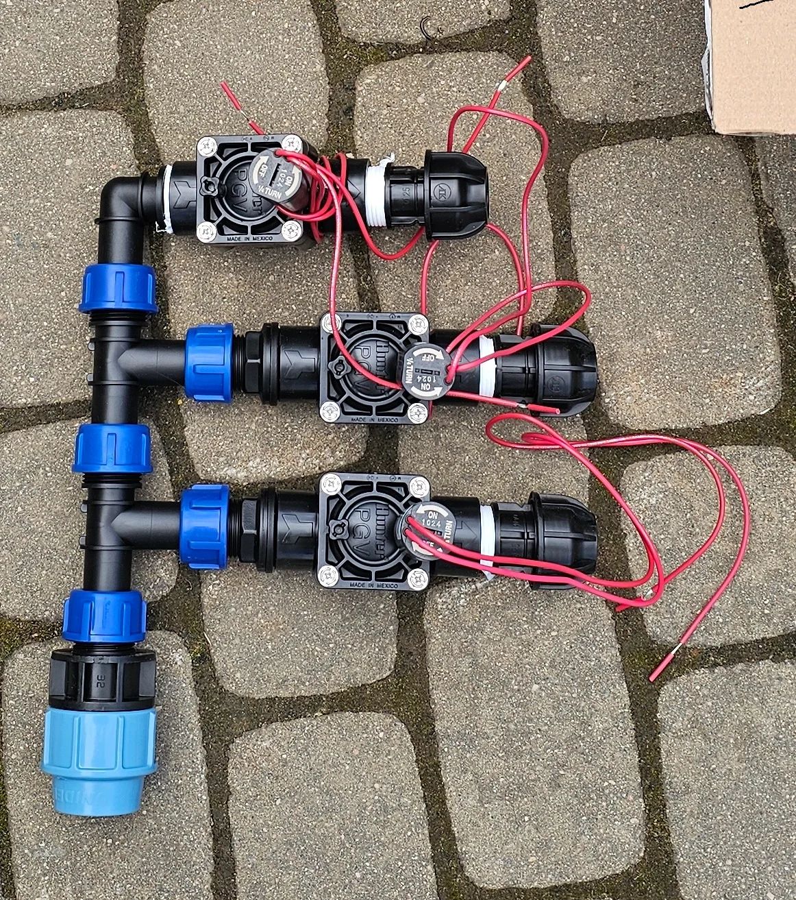 Trijų elektromagnetinių laistymo vožtuvų kolektorius su jungtimis ir laidais ant trinkelių