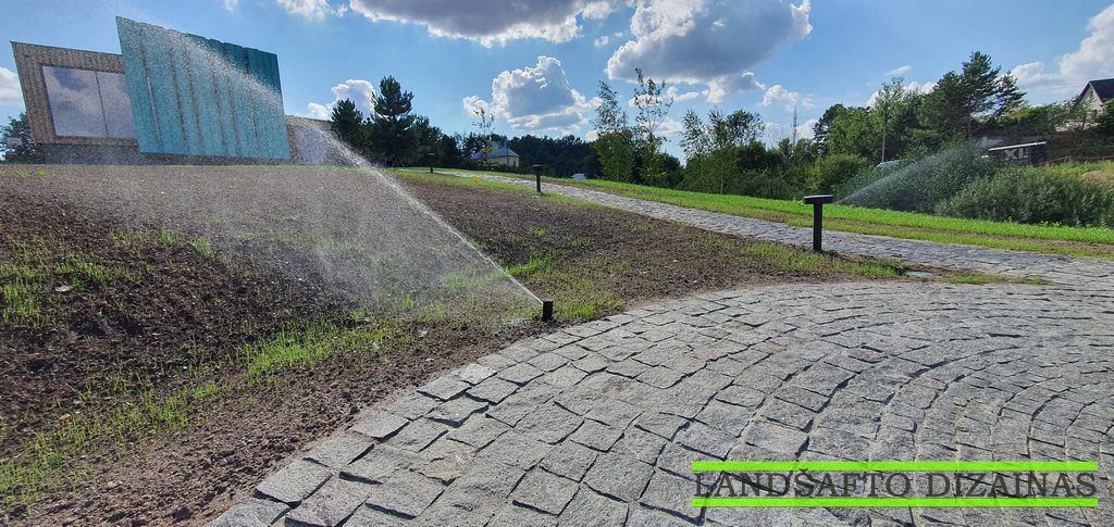 Automatinis purkštuvas laisto naujai pasėtą veją prie akmenimis grįsto tako