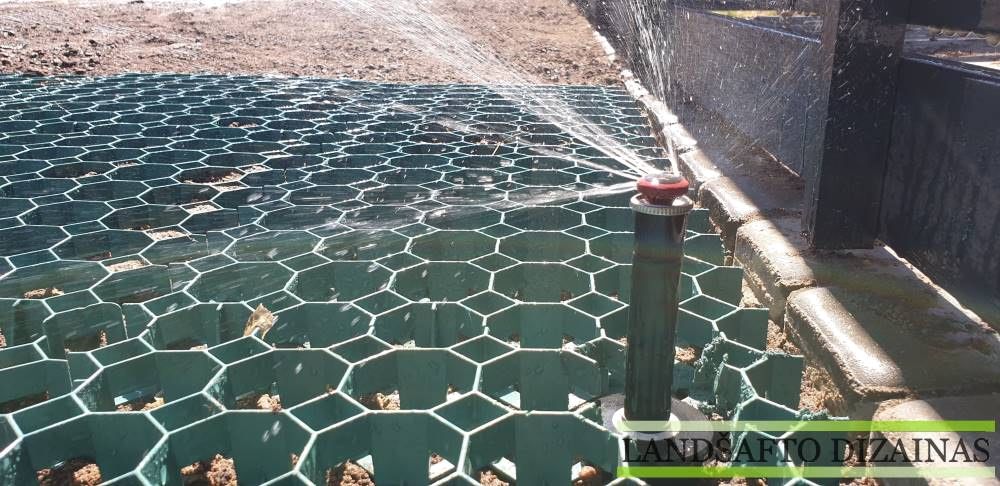 Iškilęs vejos purkštuvas purškia vandenį virš žalio plastikinio vejos korio