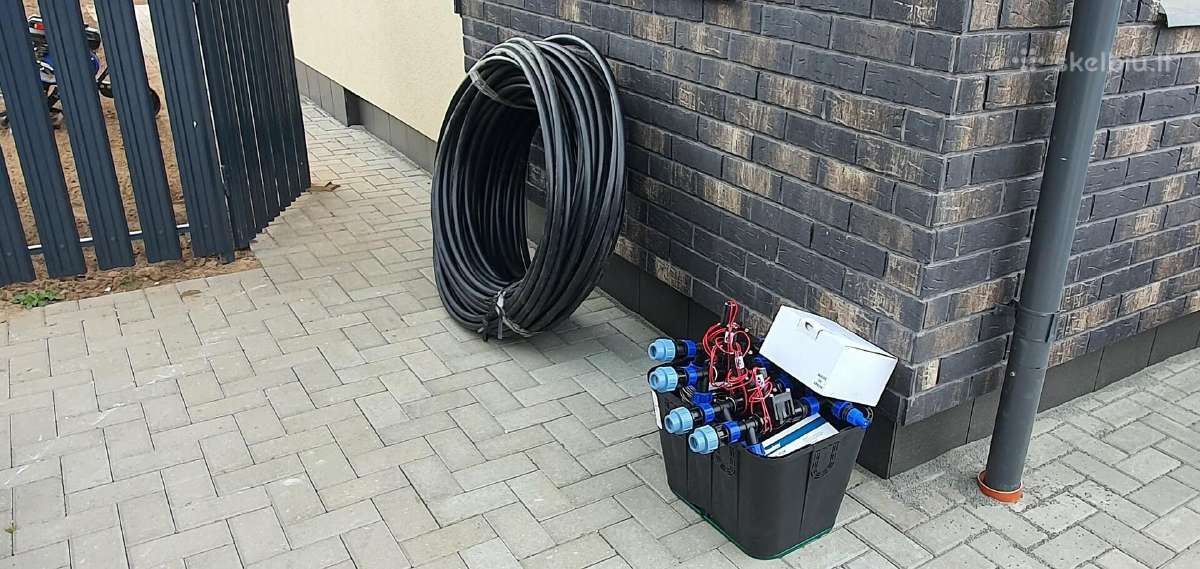 Juodo laistymo vamzdžio ritė ir elektromagnetiniai vožtuvai dėžėje prie pastato sienos